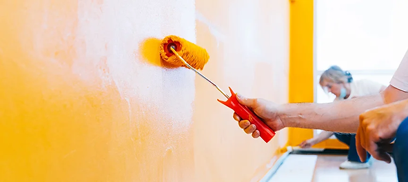 Person painting a wall with a bright orange paint roller.