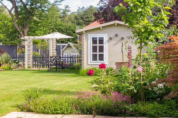 Garden with a small cottage, lush greenery, and a patio seating area under an umbrella