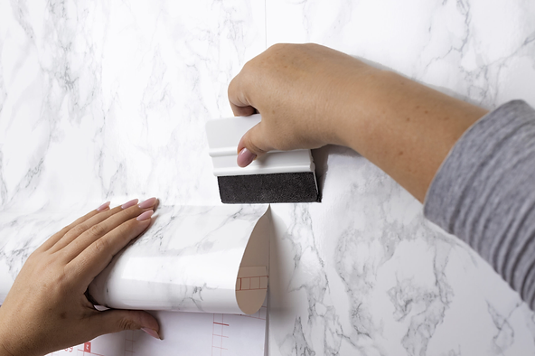 Person applying marble-patterned wallpaper with a smoothing tool.