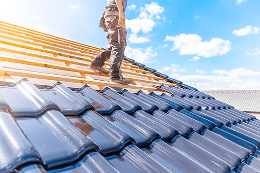 Roofer installing new tiles on a roof under a bright blue sky.